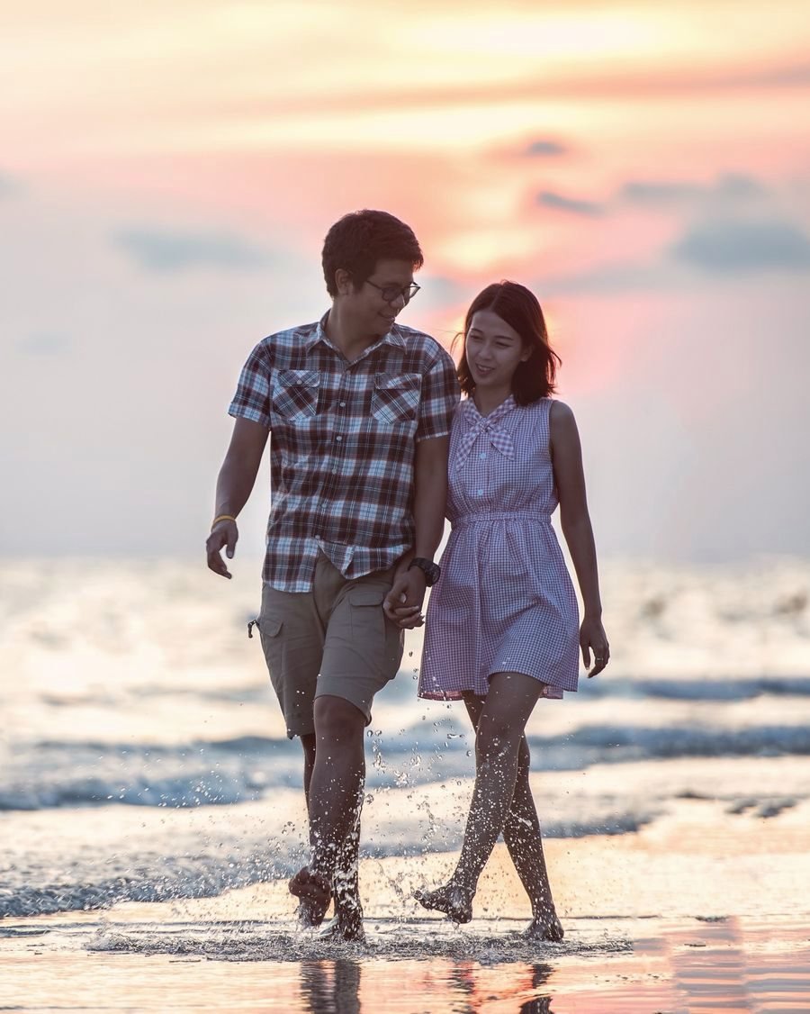 Un couple qui marche main dans la main au bord de la mer, au coucher du soleil